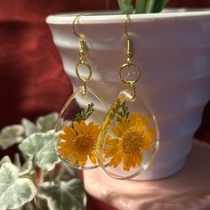 a pair of dandelion earrings sitting on top of a white potted plant