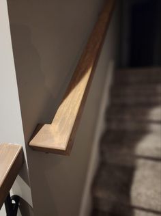 a wooden shelf sitting on the side of a white wall next to a stair case