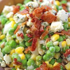 a salad with peas, corn and bacon in a wooden bowl on top of a table