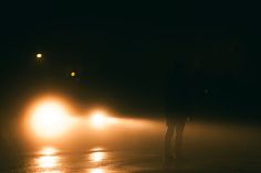 a person standing in the middle of a foggy road at night with headlights on