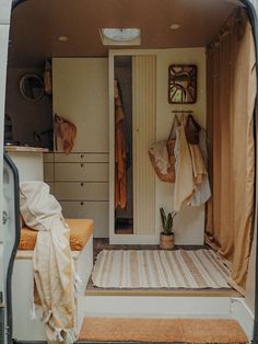 the inside of a camper van with clothes hanging on it's doors and shelves