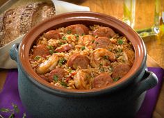 a bowl of food sitting on top of a wooden table next to bread and wine glasses