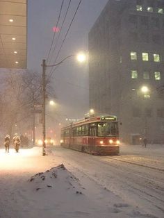 a city street covered in snow with people walking on the sidewalk and cars driving down it