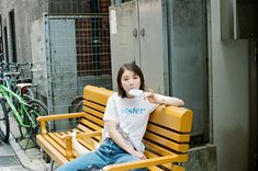 a woman sitting on a yellow bench in front of a building with bicycles behind her