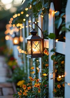 a lantern is hanging on the side of a white fence with flowers and lights around it