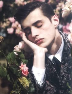 a man with his hand on his face next to some pink flowers and greenery