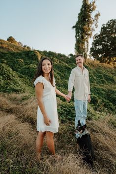 a man and woman holding hands while standing next to a black dog on a hill