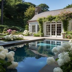 a pool surrounded by white flowers next to a house with large windows and lots of greenery