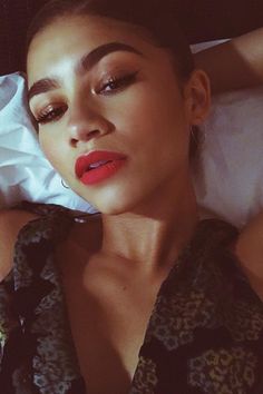 a woman laying on top of a bed next to a white sheet covered wall and wearing red lipstick