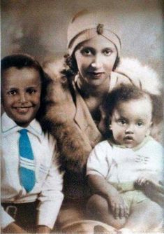 an old photo of two women and a baby in front of a backdrop with feathers on it