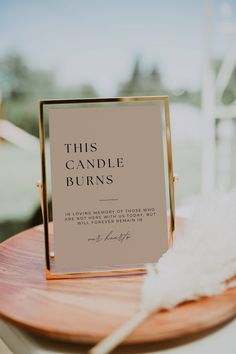 this candle burns sign is on top of a wooden table with feathers in the background