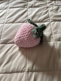 a pink crocheted strawberry laying on top of a white bed sheet with green leaves