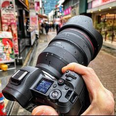 a person holding up a camera in front of a street with stores on the sidewalk