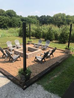 an outdoor fire pit surrounded by lawn chairs and graveled area with trees in the background