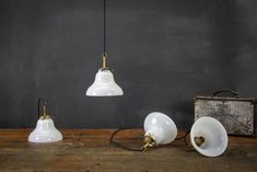 three white light fixtures on a wooden table next to an old suitcase and lamp shade