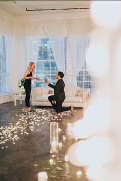 a woman kneeling down next to a man in front of a couch with candles on the floor