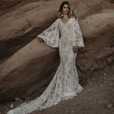 a woman standing in front of rocks wearing a white lace wedding dress with bell sleeves