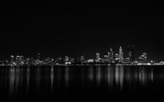 black and white photograph of the city skyline at night from across the water with reflections on the surface