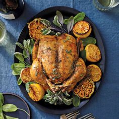 a roasted turkey on a black plate with oranges and sage leaves next to it