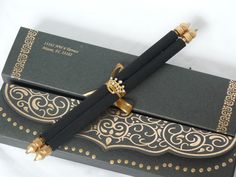 a pen sitting on top of a black box with gold trimmings and an ornate design