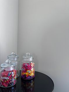 two glass jars filled with candy sitting on top of a black table next to a white wall