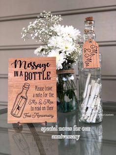 a message in a bottle next to a vase with white flowers and an acrylic sign