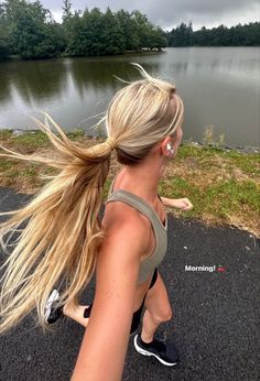 a woman running down the road with her hair blowing in the wind and water behind her