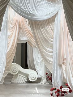 a white bed covered in draping and flowers on top of a floor next to a wall