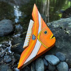 an origami fish sitting on top of rocks next to a body of water