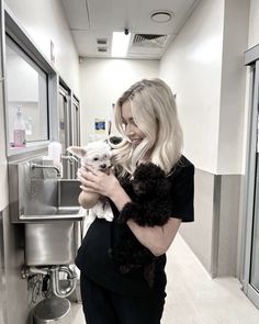 a woman is holding a small dog in her arms while standing next to a sink