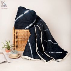 a basket with a book and a blanket on it sitting next to a plant in a vase