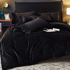 a bed with black comforter and pillows in a dark room next to a chair