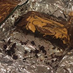 a piece of cake sitting on top of tin foil covered in chocolate and yellow frosting