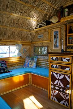 the inside of a hut with wood flooring and thatched roof, blue cushioned bench