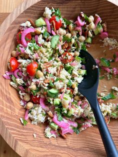 a salad in a wooden bowl with a black spoon on the side, ready to be eaten