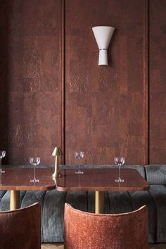 two chairs and a table with wine glasses on it in front of a brown wall