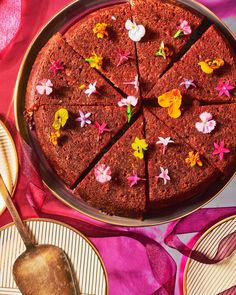 a chocolate cake with flowers on it sitting on a table next to plates and utensils