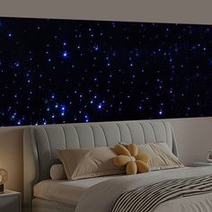 a bed sitting under a night sky with stars on the wall and pillows in front of it