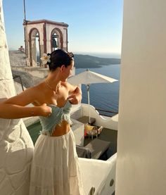 a woman standing on top of a roof next to the ocean wearing a white dress