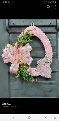 a pink wreath is hanging on the front door with a bow and ribbon around it