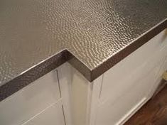 a kitchen counter top that is made out of metal and white cabinets with wood flooring