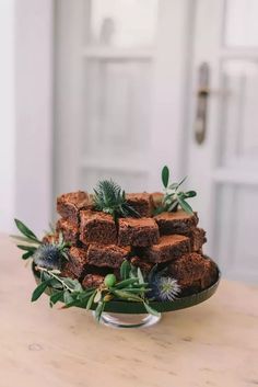 some brownies are stacked on a plate with green leaves and sprigs in front of them