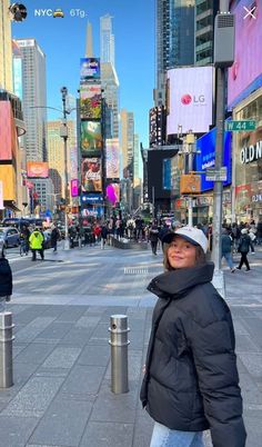 a woman standing in the middle of a busy city street with tall buildings and billboards