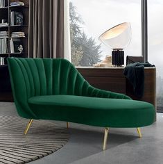 a green chair sitting in front of a window next to a book shelf and lamp