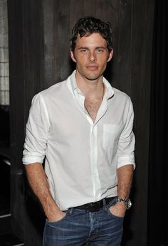 a man standing in front of a wooden wall wearing a white shirt and blue jeans