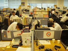 an office filled with people working on their computers and desks full of books, papers