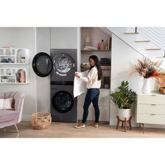 a woman is standing in front of a washer and dryer with her hand on the door