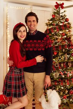 a man and woman standing in front of a christmas tree with their arms around each other