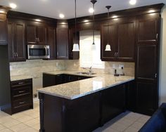 a kitchen with dark wood cabinets and granite counter tops, along with white tile flooring