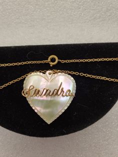 "This piece is from the 1930's and most likely were premiums at tourist areas like fairs. This one is specialized for Sandra. It's made of iridescent white Mother of pearl in the shape of a heart with the original curb chain. This information I got from my book title \"Brilliant Rhinestones Vintage & Contemporary Jewelry\" from the Ronna Lee Collection page 73.  The majority of them had \"MOTHER\" in cursive. This one came from my collection which I've had for decades. It will arrive in a gift b Collectible Heirloom Necklace For Valentine's Day, Collectible Heart-shaped Hallmarked Jewelry, Vintage Necklaces For Valentine's Day Memorial, Vintage Necklace For Valentine's Day Memorial, Engraved Jewelry Collectible For Valentine's Day, Personalized Heart Jewelry Collectible, Personalized Heart Jewelry For Collectors, Vintage Nameplate Necklaces, Victorian Personalized Jewelry For Valentine's Day